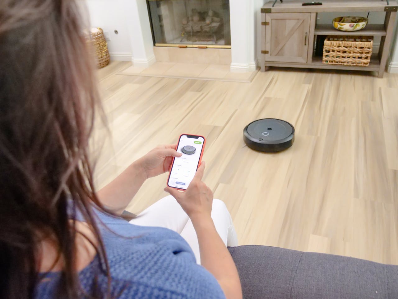 hero-img-02 Overhead view of a woman controlling a robot vacuum using a smartphone app on a wooden floor.